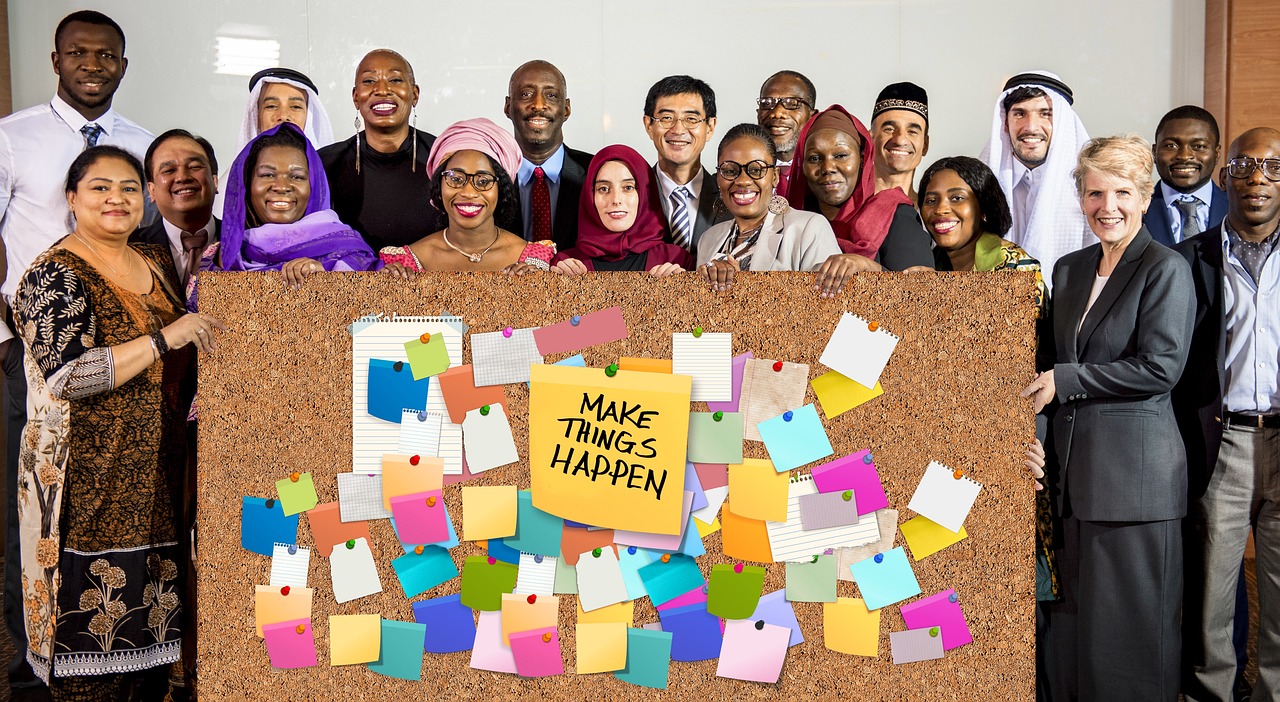 Equipe sorridente reunida em frente a um quadro de recados cheio de post-its coloridos, planejando o projeto